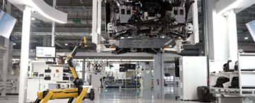 Yarı zamanda iki kat iş yazısı için görsel: aydınlık bir fabrika zemininde yürüyen dört bacaklı sarı robot