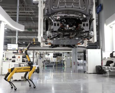 Yarı zamanda iki kat iş yazısı için görsel: aydınlık bir fabrika zemininde yürüyen dört bacaklı sarı robot