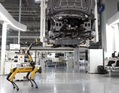 Yarı zamanda iki kat iş yazısı için görsel: aydınlık bir fabrika zemininde yürüyen dört bacaklı sarı robot