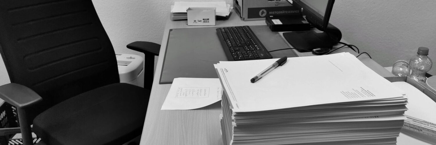 Boş bir ofis sandalyesinin yanında üst üste yığılmış kağıtlarla dolu masa