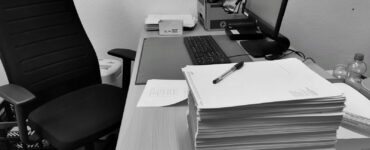 Boş bir ofis sandalyesinin yanında üst üste yığılmış kağıtlarla dolu masa