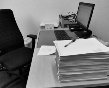 Boş bir ofis sandalyesinin yanında üst üste yığılmış kağıtlarla dolu masa