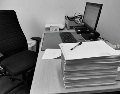 Boş bir ofis sandalyesinin yanında üst üste yığılmış kağıtlarla dolu masa