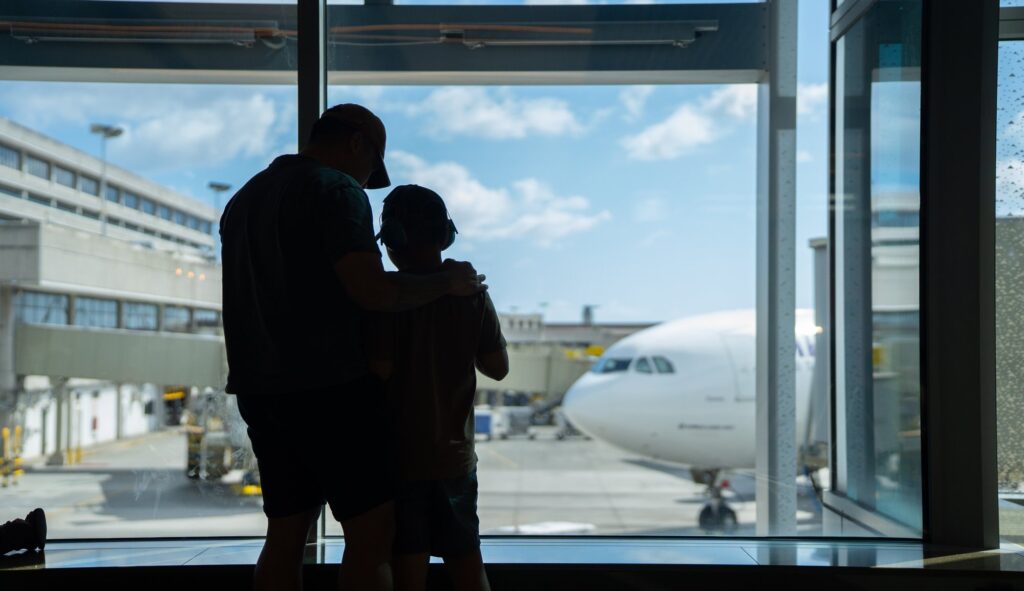 Honolulu Havalimanı'nda bir baba ve oğlu kapı bölümündeki camın önünde apronda bekleyen Hawaiian Airlines uçağına bakıyor