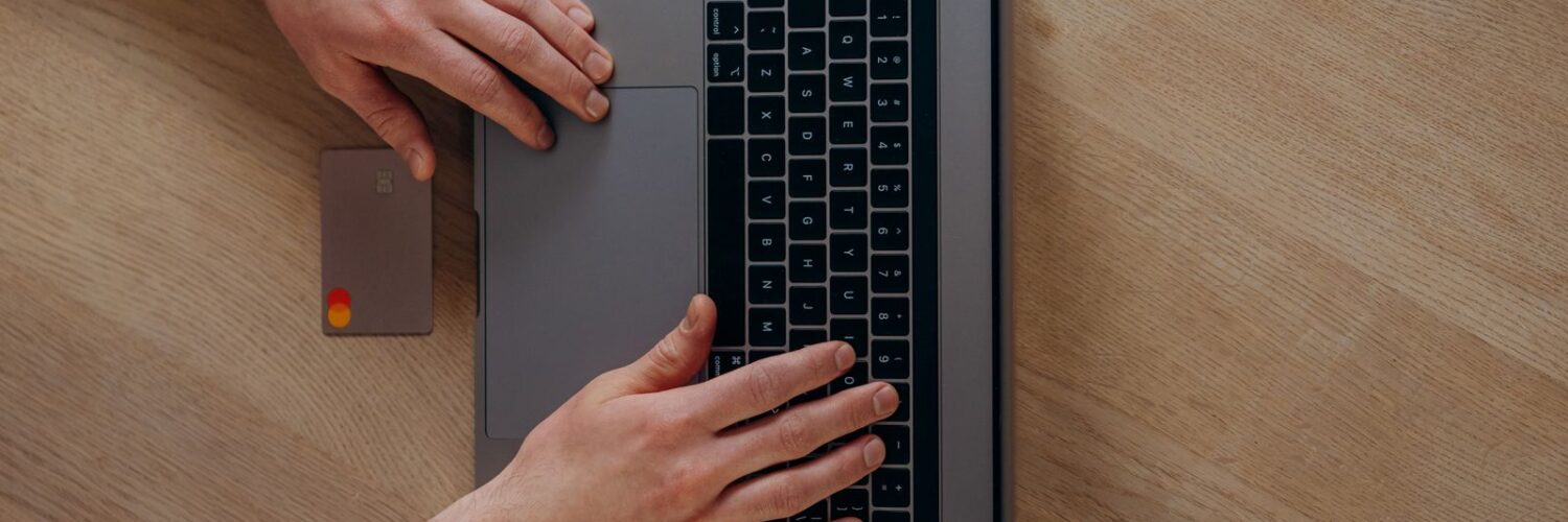 Ahşap masada dizüstü bilgisayar ve kredi kartıyla online alışveriş yapan biri