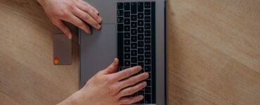 Ahşap masada dizüstü bilgisayar ve kredi kartıyla online alışveriş yapan biri