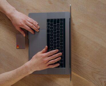 Ahşap masada dizüstü bilgisayar ve kredi kartıyla online alışveriş yapan biri