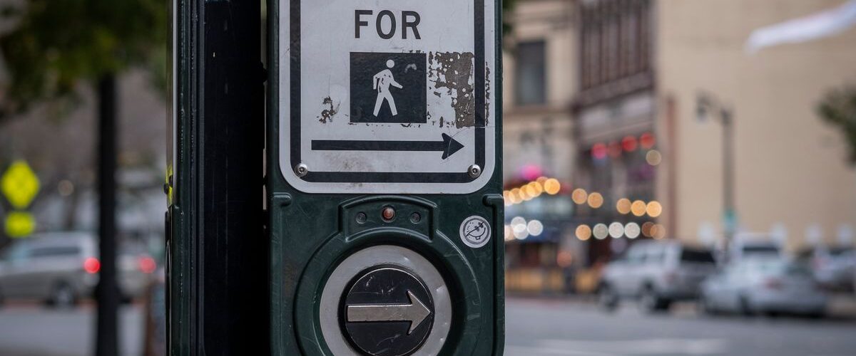 Bir direkteki yıpranmış yaya geçidi düğmesi, arkada bulanık bir cadde